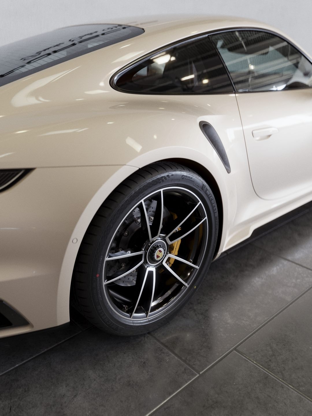 Rear wheel and side air intake of a light grey Porsche on a dark tiled floor