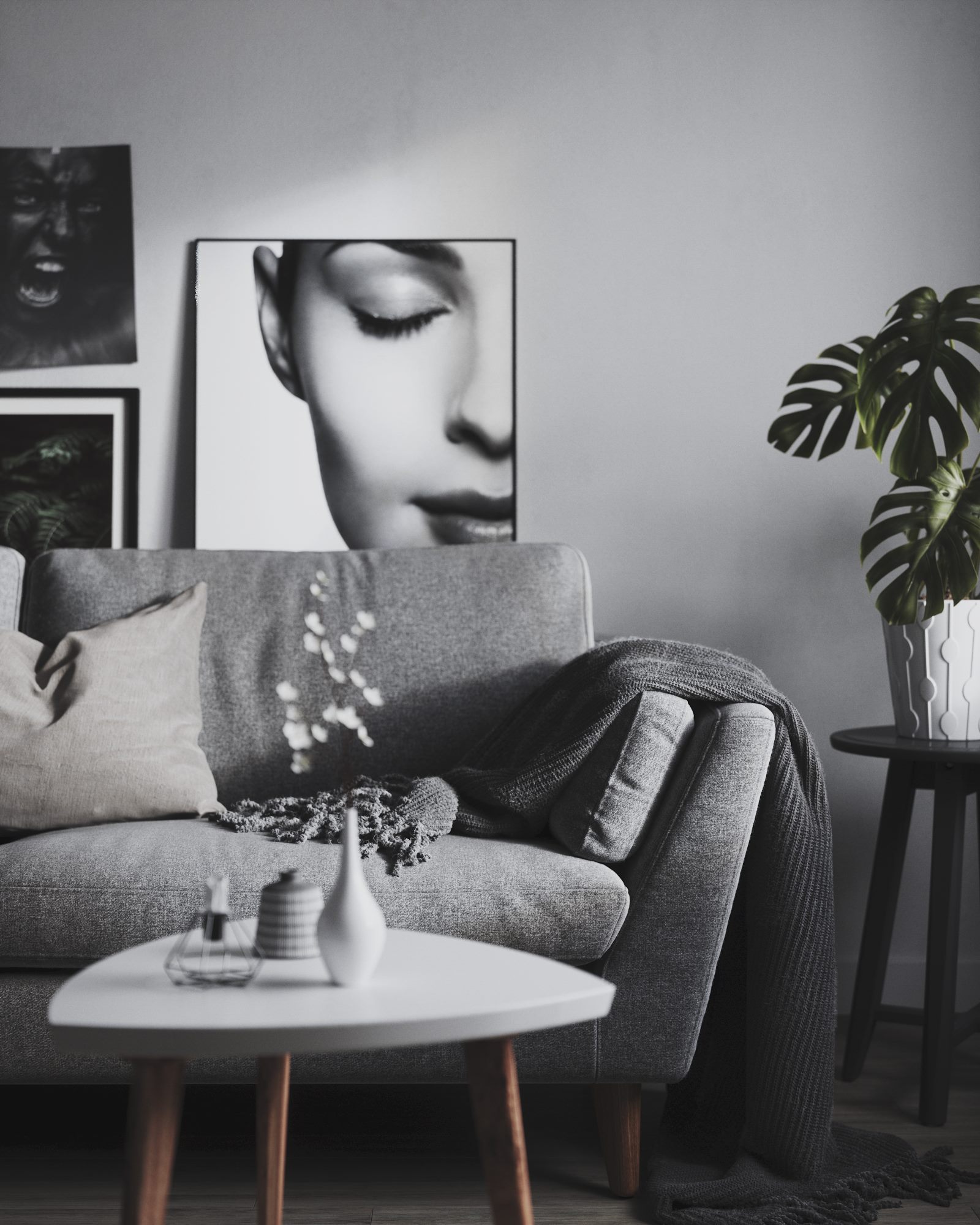 Grey sofa with cushions, a round white coffee table, a plant and a black and white portrait on the wall